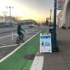 person riding bike on green bike path past Ferry Building and Quick Build sandwitch board