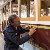 A painter lays down masking tape to paint striping on the side of Powell St. Cable Car 22,
