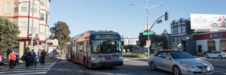 38 Bus Merging into Traffic on Geary Boulevard with pedestrians crossing sidewalk on left. 