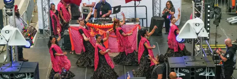 Performers in South Asian dress on a stage with a band in front of an audience. A banner above the stage reads "Bhangra and Beats Night Market"