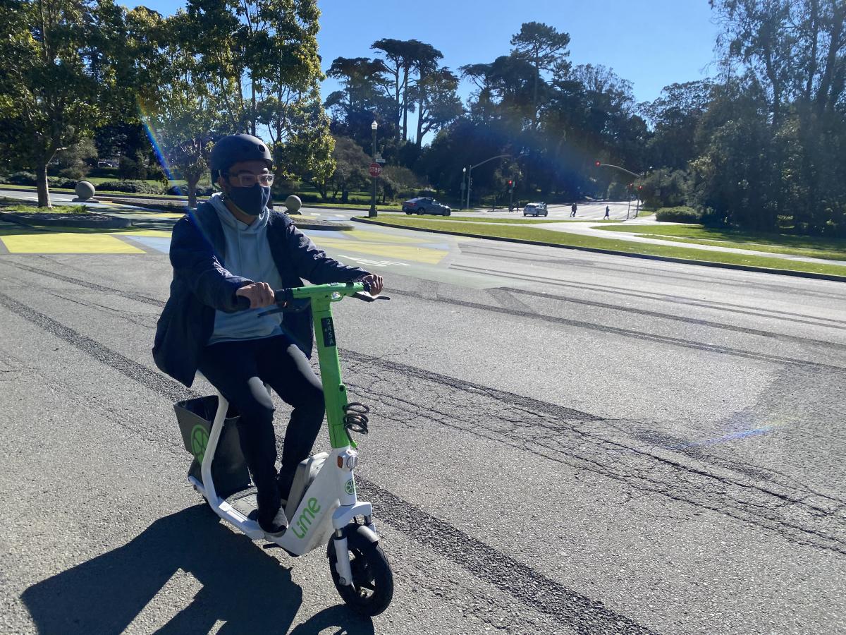 Person rides a lime green shared scooter through Golden Gate Park.