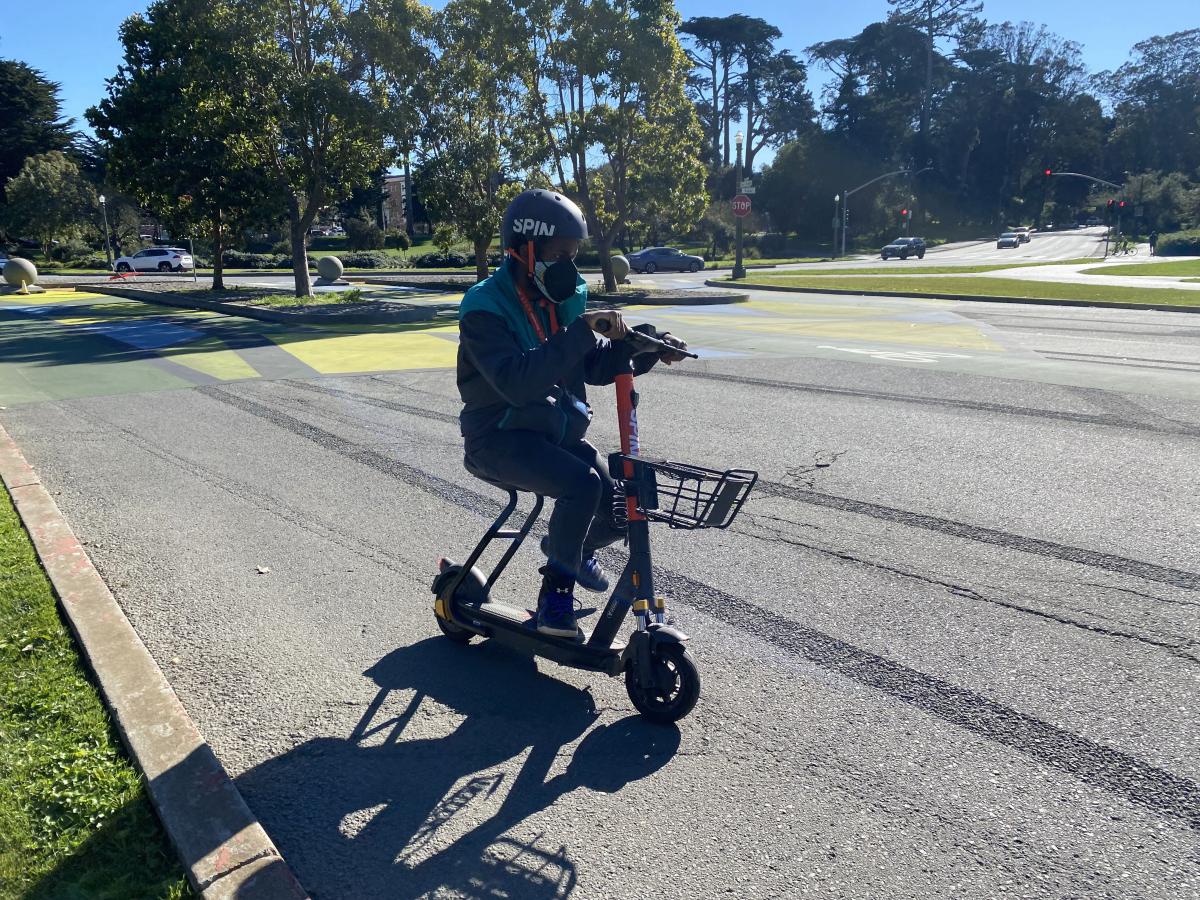 Person rides a shared scooter that features a basket through Golden Gate Park.