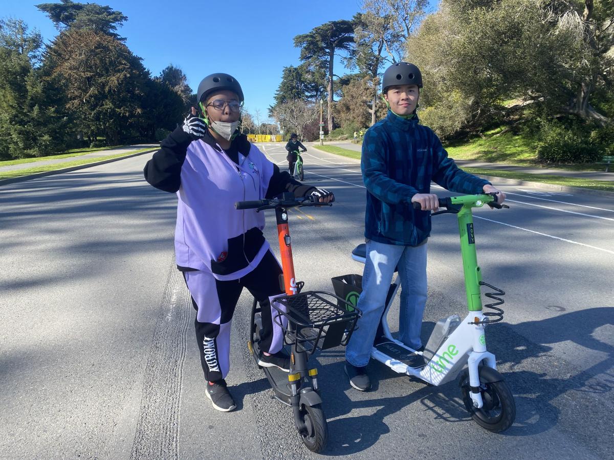 Students smile while riding shared scooters with accessibility features.