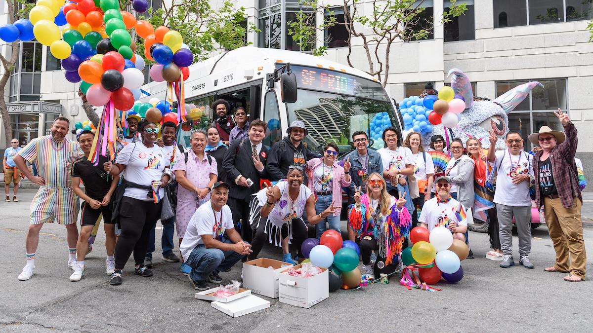 SFMTA staff, family and friends gather for a photo in front of a Muni bus at the SF Pride Parade.