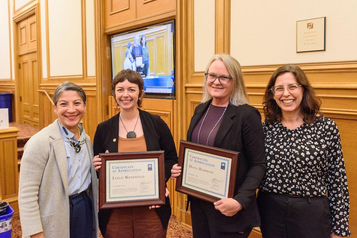 Four women standing with two holding certificates.