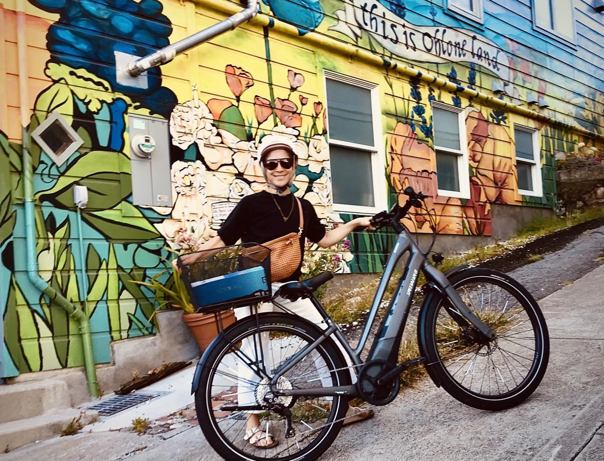A woman standing with a bicycle in front of a mural. 