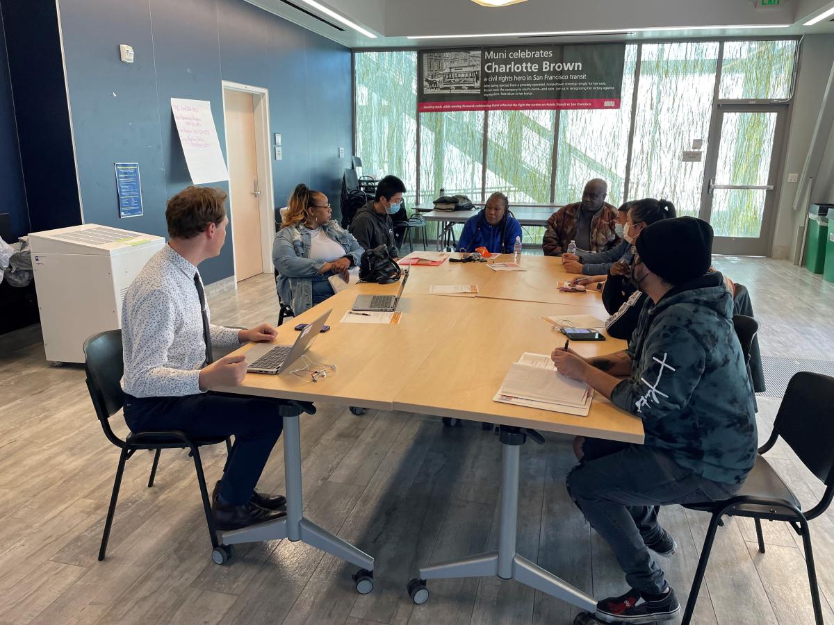 SFMTA staff and community partners sit at a table and chat in a conference room.