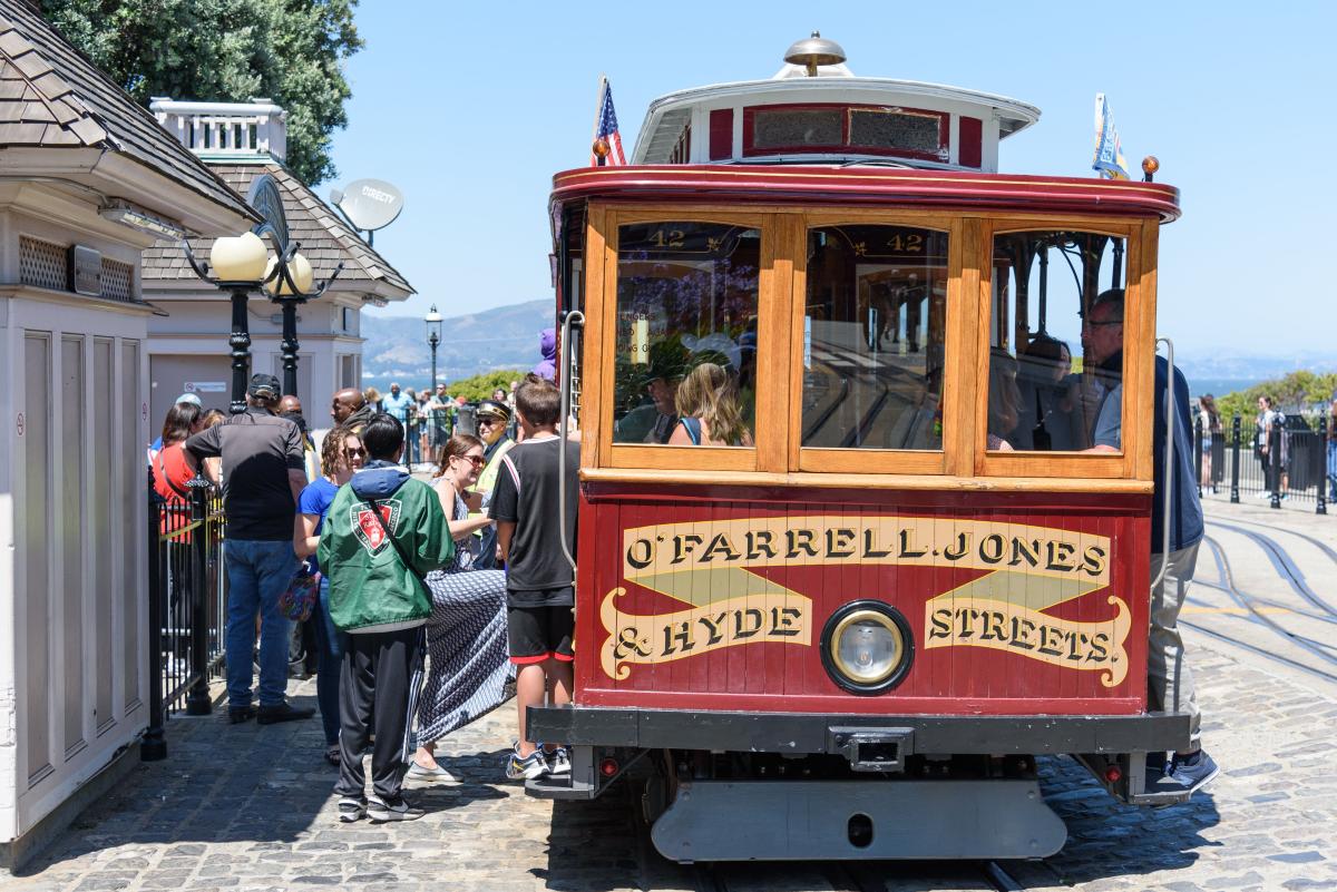 Cable car with sign that says "O'Farrell, Jones & Hyde Streets" picks up riders near Aquatic Park. 