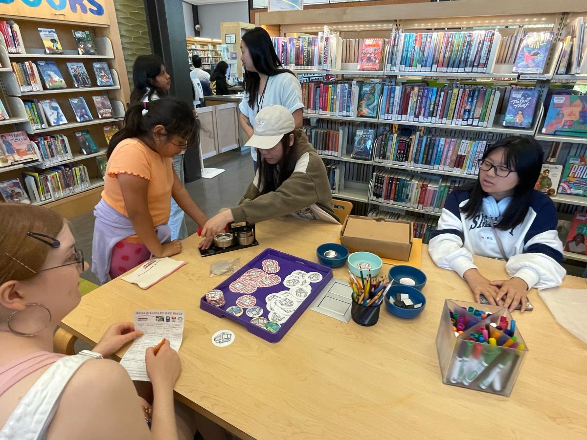 Young people sit at a table and make crafts in a library.