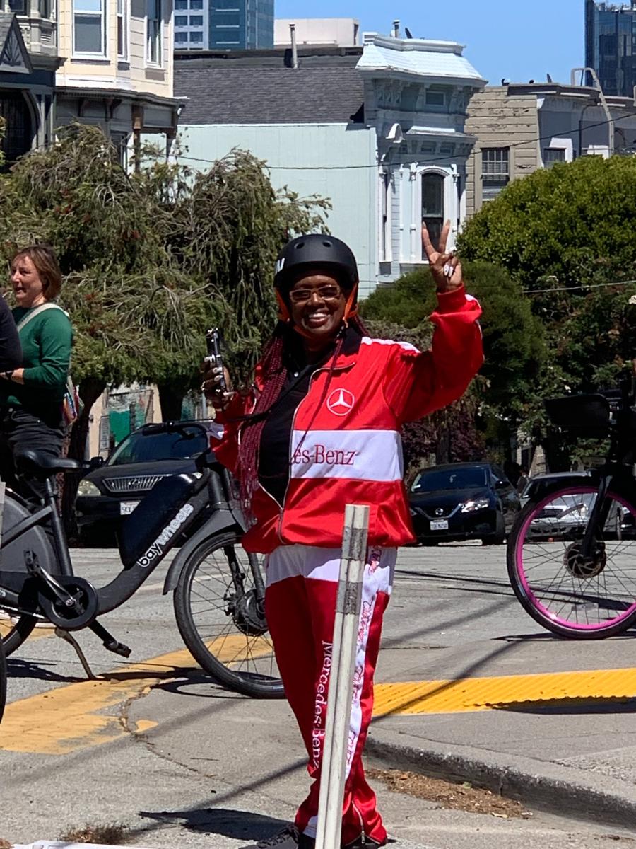 Person holds peace sign while standing in intersection where people nearby ride bikes.