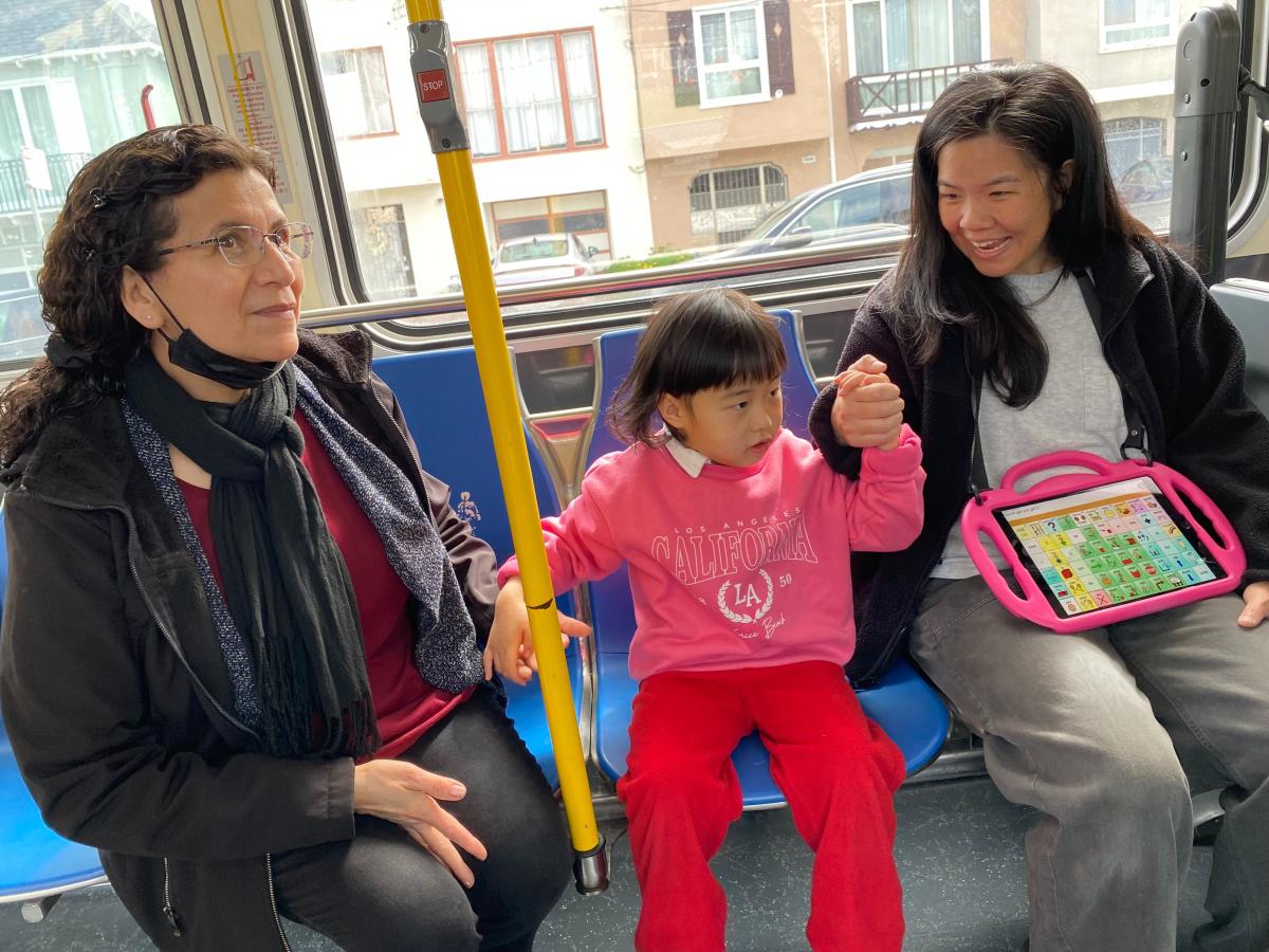 A young child holds hands with two adults on a bus. 