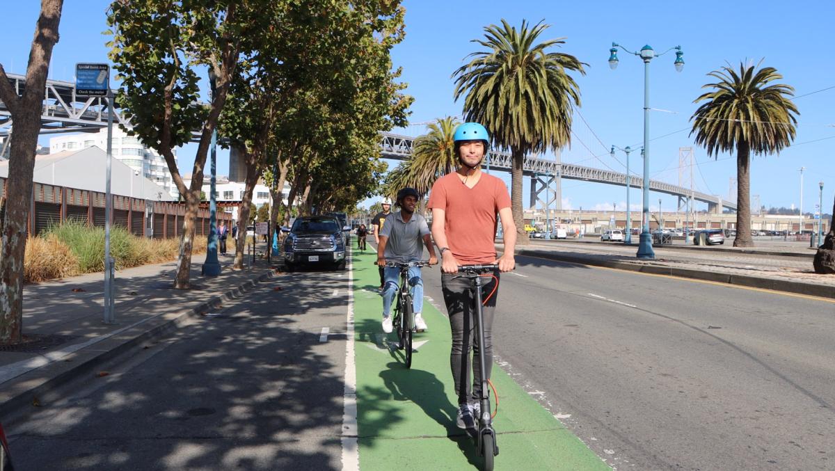 Two people ride scooters in a bikeway that's painted green by the Embarcadero.