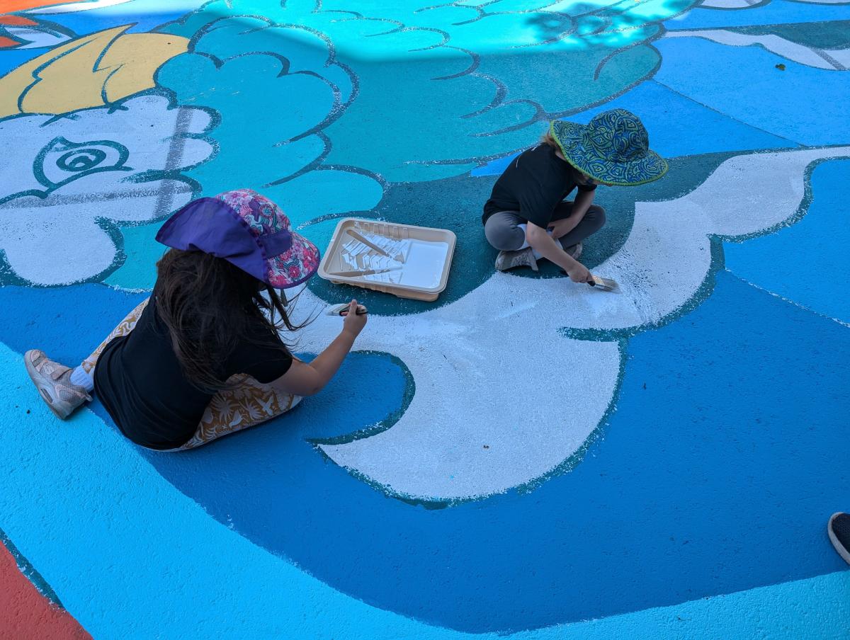 Two children painting on a blue and white surface on the street - the Lyon Slow Street mural.