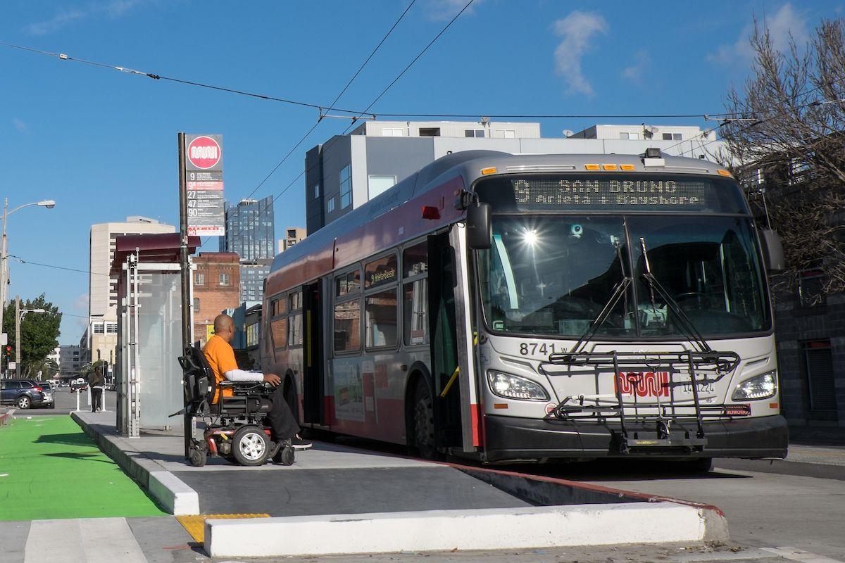 A photograph of a person using a wheelchair who is preparing to board the 9 San Bruno on a boarding island. 