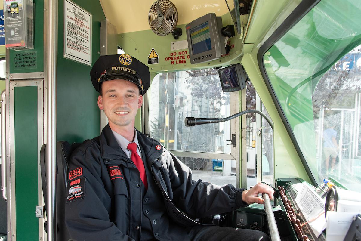 Mike Delia smiles broadly as he wears a vintage eight-point cap and sits in the operator’s seat of a historic streetcar.