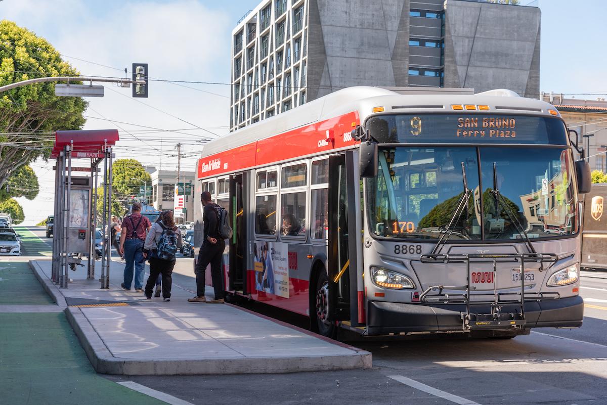 A photograph of Muni riders exiting the 9R San Bruno Rapid onto a boarding island on Potrero Avenue. 