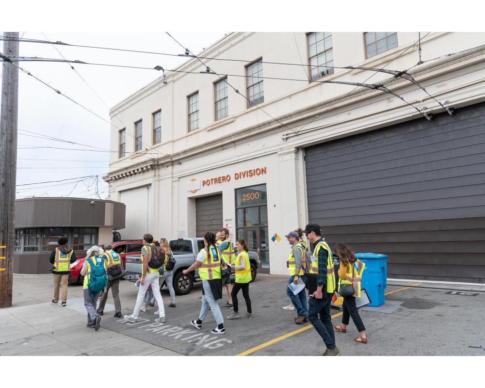 Several people wearing yellow safety vests begin a tour outside the Potrero Yard.