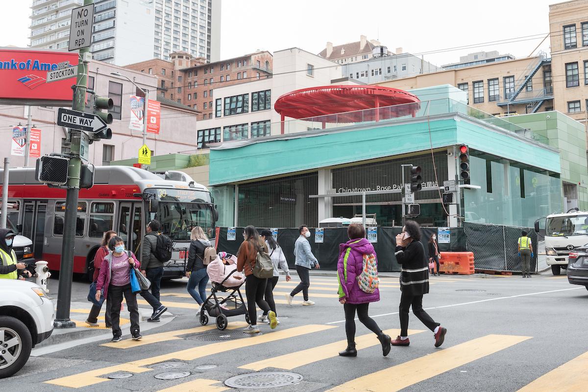 A photograph of the 30 Stockton passing the Chinatown-Rose Pak metro station on Stockton Street in San Francisco with pedestrians crossing the street. 