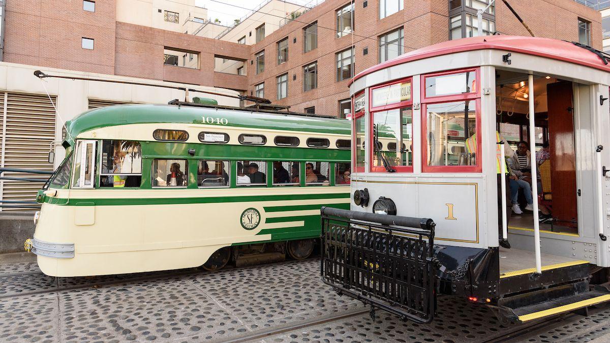 Two retro streetcars, one cream and green and one gray and red, pause during Muni Heritage Weekend 2023.