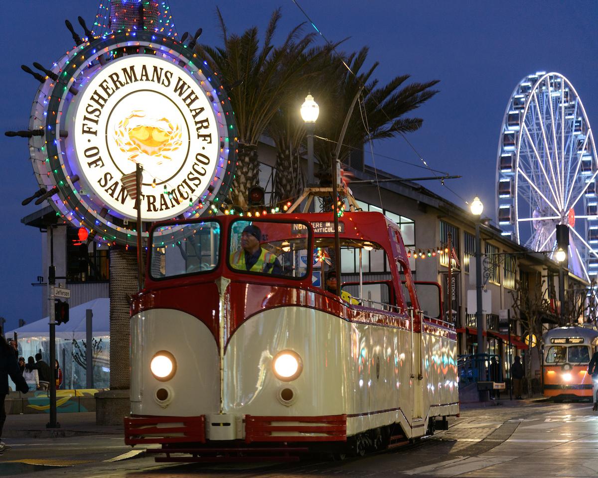 An open air streetcar in front of a bright sign and a Ferris wheel.