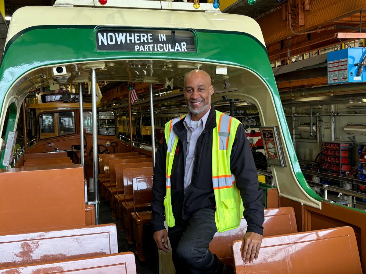 Muni Operator David Gunter in a yellow vest on a vehicle with wooden seats.