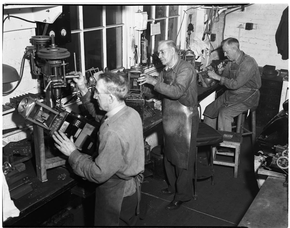 Black and white photo of shop mechanics repairing fare boxes for Muni in the 1940's.