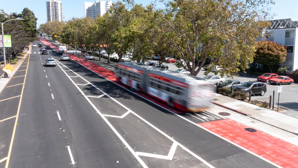 A bus uses a red transit-only lane near cars on a busy street