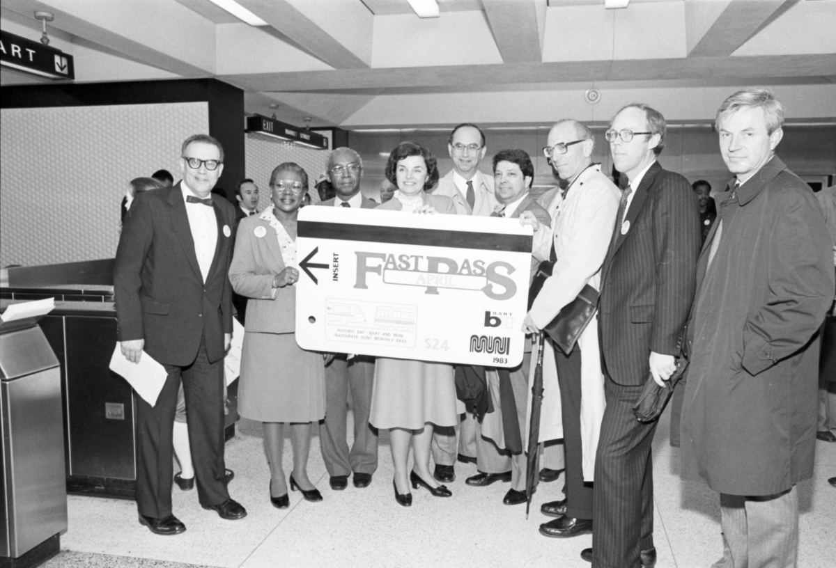 Archival photo in black and white that features former San Francisco Mayor Dianne Feinstein in Civic Center Station helping to promote a type of Fast Pass along with other officials at a press conference.