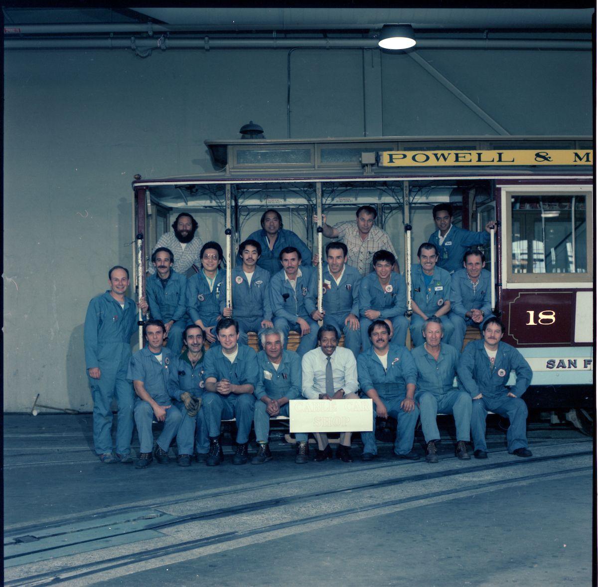 A photo of the cable car shop crew taken in 1986. All of the people pictured in the photograph are men.