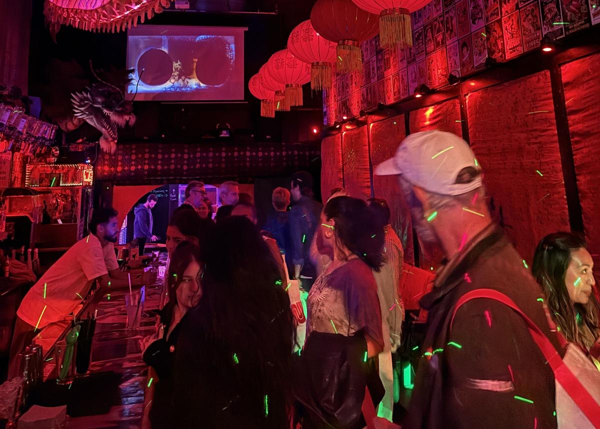 People in a room with a long bar and red lighting.