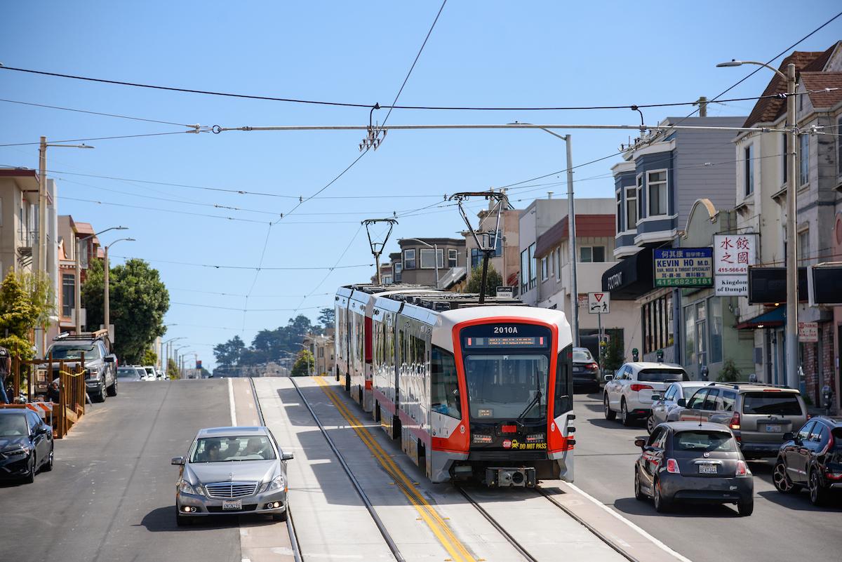 An L Taraval train heads down a hill as cars use nearby lanes.