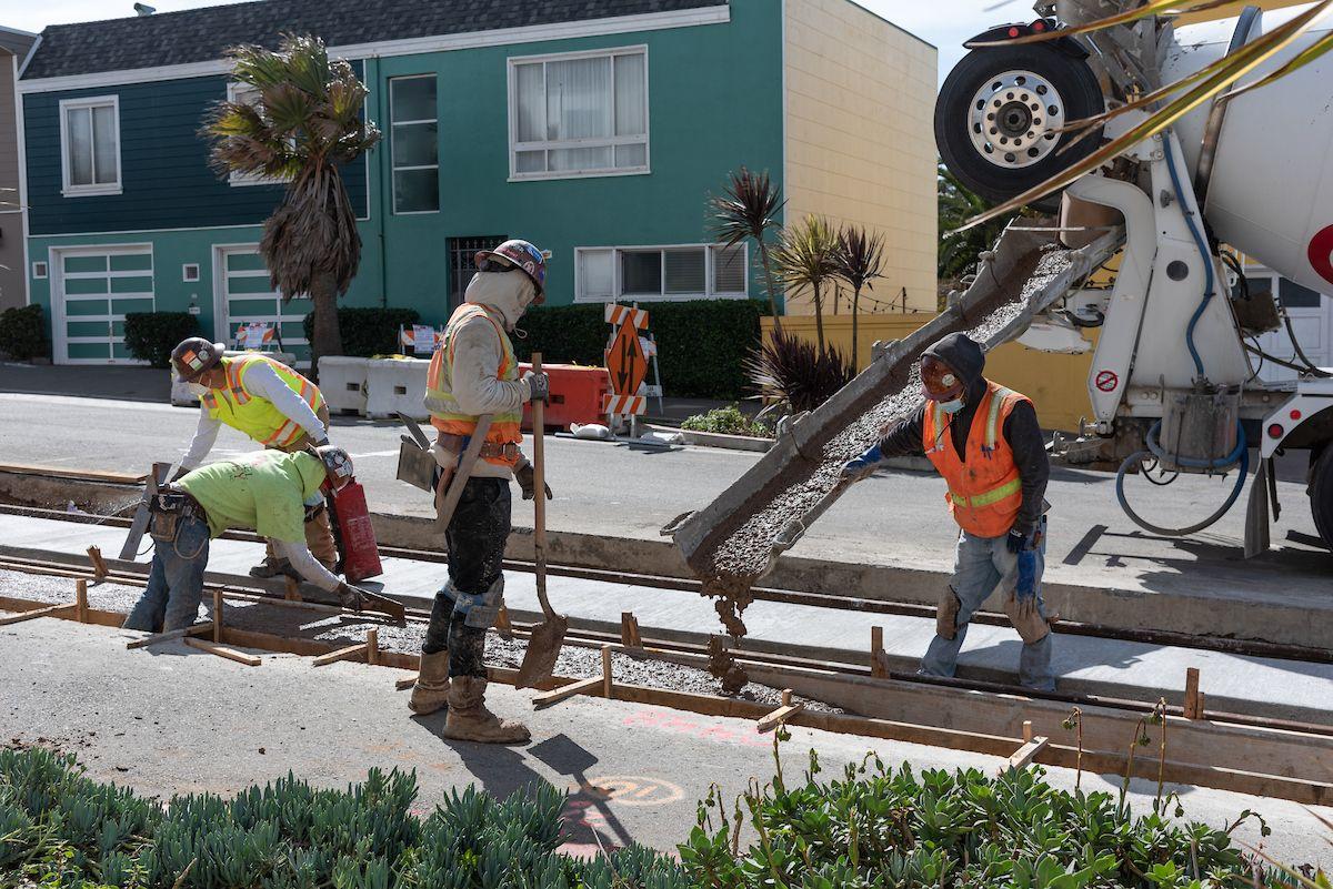 Four people wearing safety vests pour concrete for track replacement along the L Taraval Line.