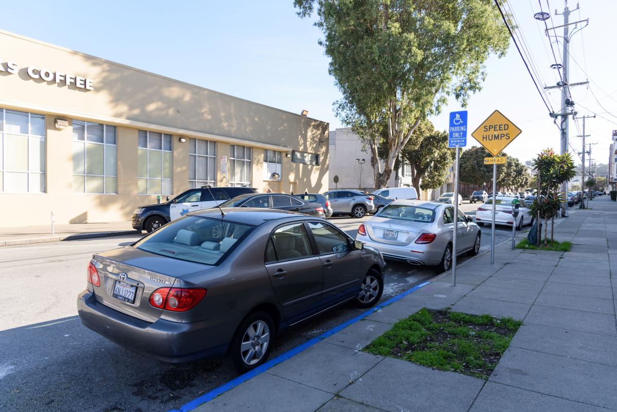 Car parked next to a curb that's painted blue. A sign also indicates that it's an accessible parking space.