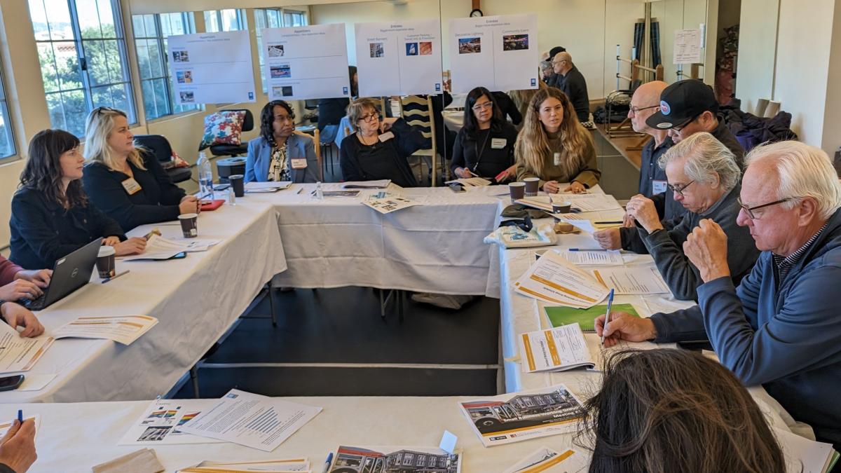 Several people sit around a set of tables covered in white table cloth during a meeting of the Geary Small Business Working Group.