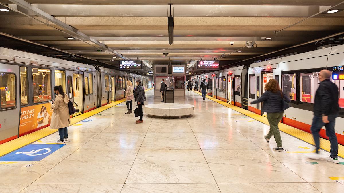 People leaving and waiting to board Muni trains at a station platform.