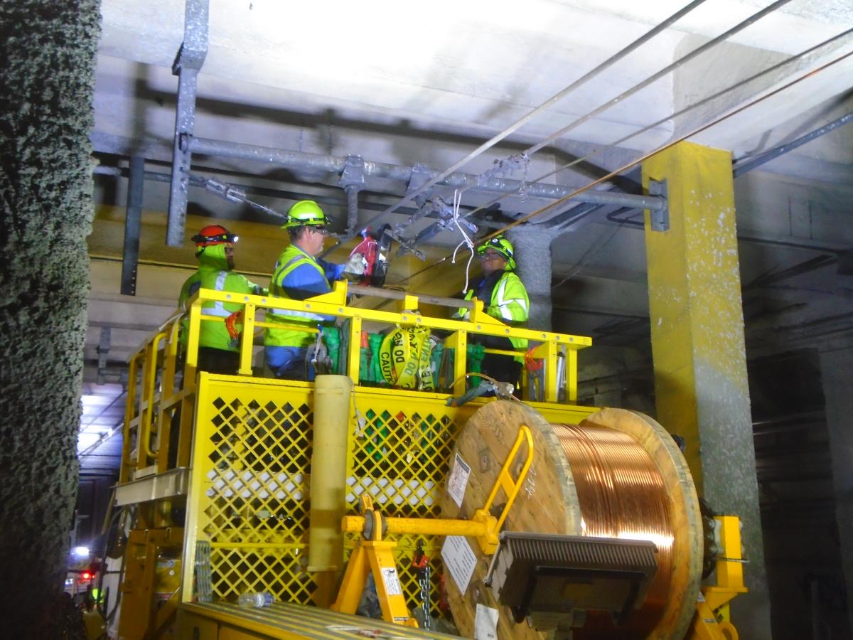 Crews wearing hard hats and yellow safety vests work on overhead lines.