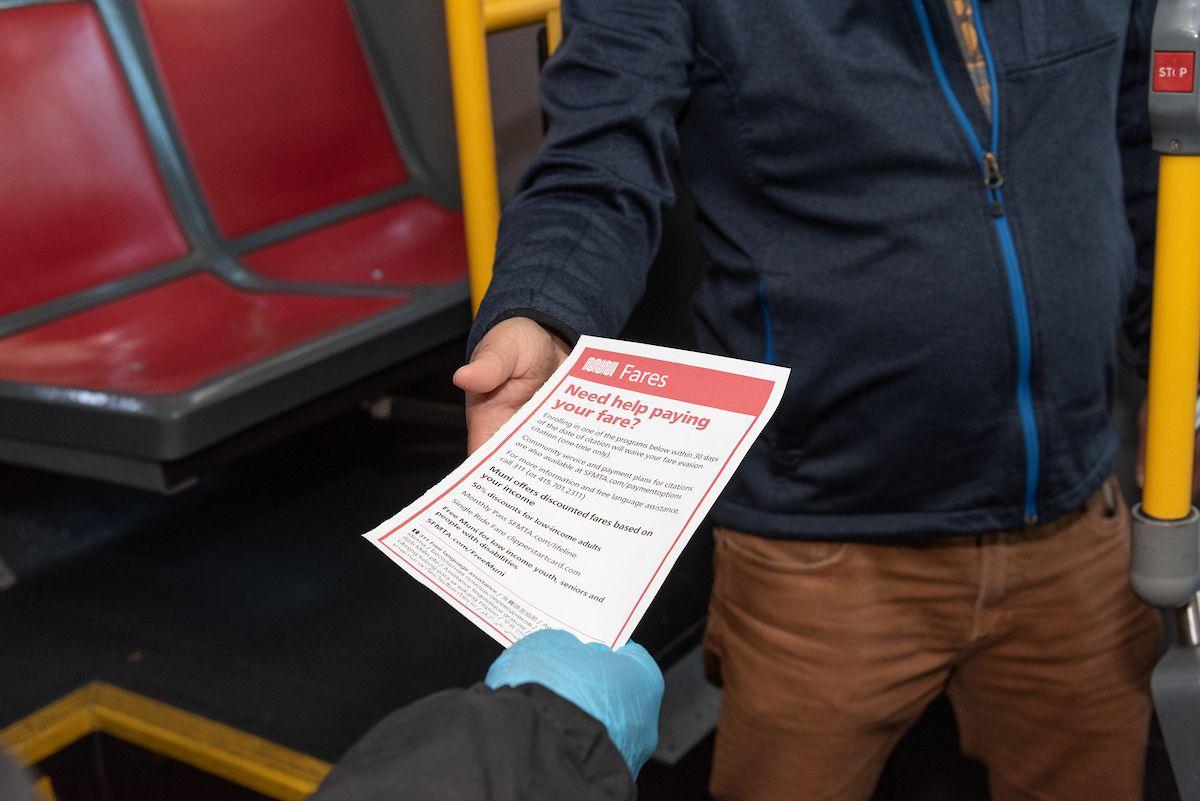 A hand giving a red and white card to someone on a transit vehicle