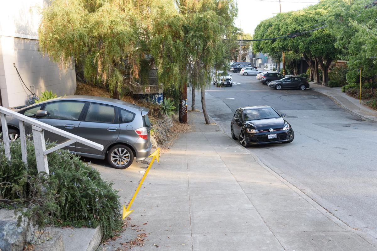 Image shows a vehicle parked legally in a driveway, with a yellow arrow illustrating that the car does not block the sidewalk.