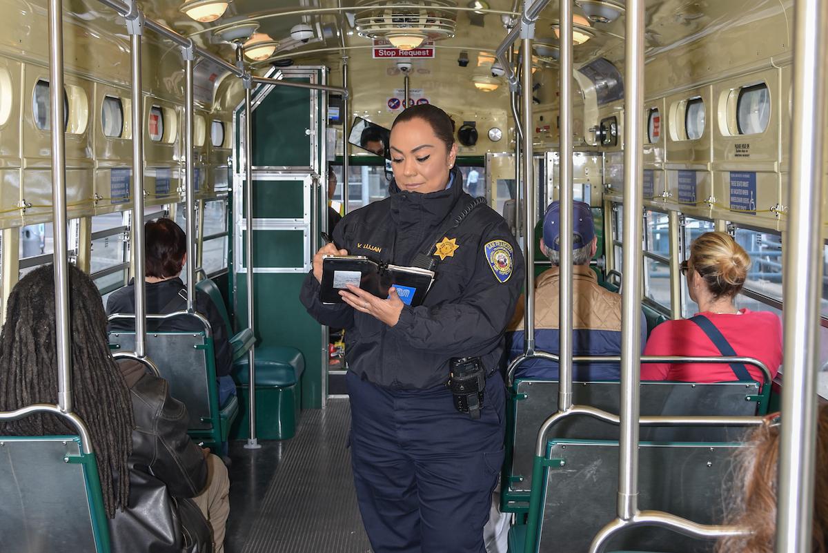 A woman standing on a transit vehicle with other people sitting on the vehicle. 