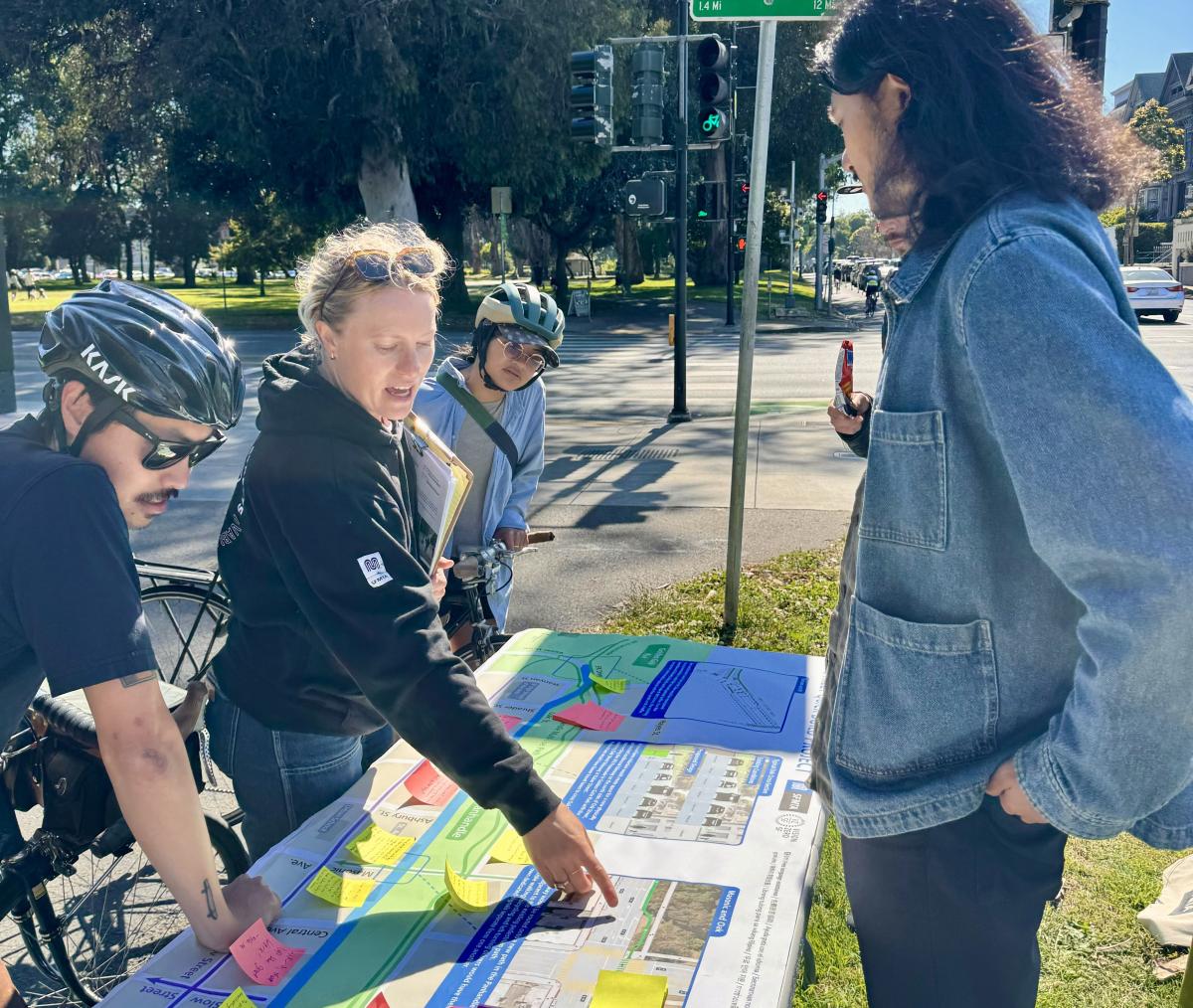 Image of SFMTA staff and community members discussing the Oak Quick-Build plans while looking at a map of proposed changes during a pop-up event outside at Oak & Masonic