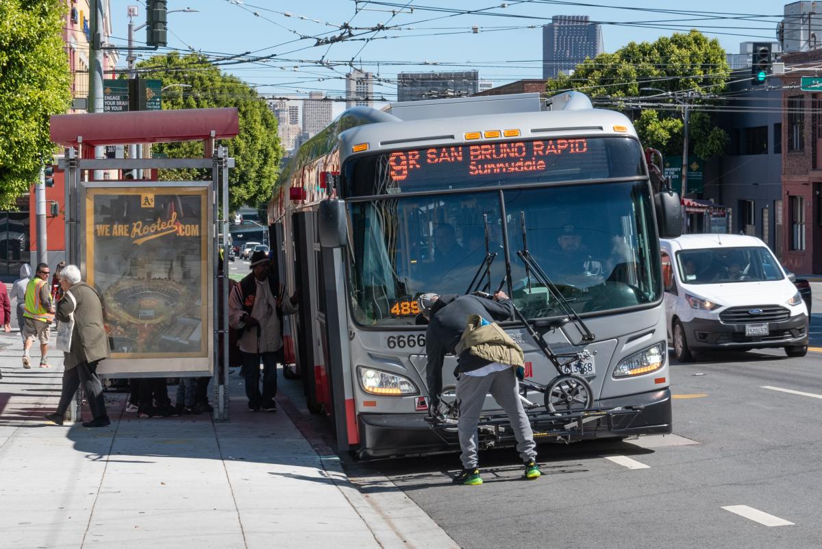 Person puts their bike on a rack in front of a 9R San Bruno Muni bus.