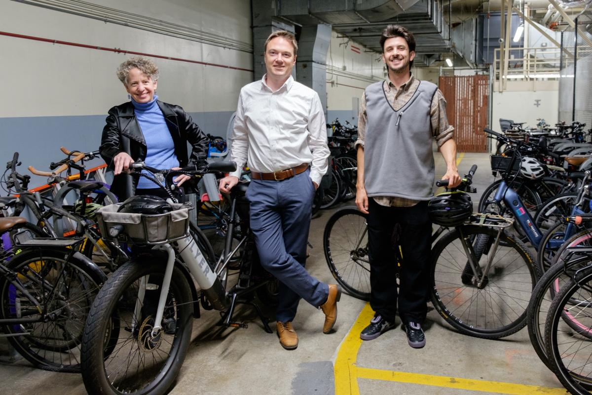 Three people stand near dozens of bikes in a bike storage area.