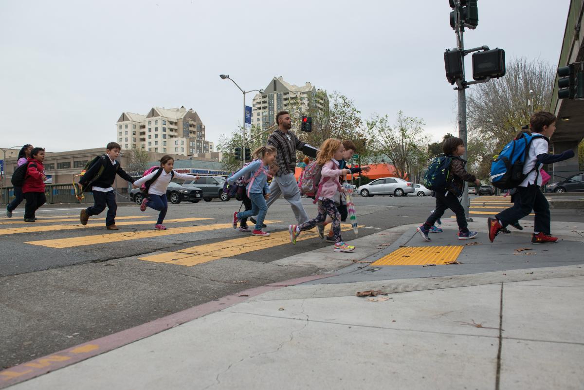 Several students and an adult cross a marked yellow crosswalk in San Francisco.