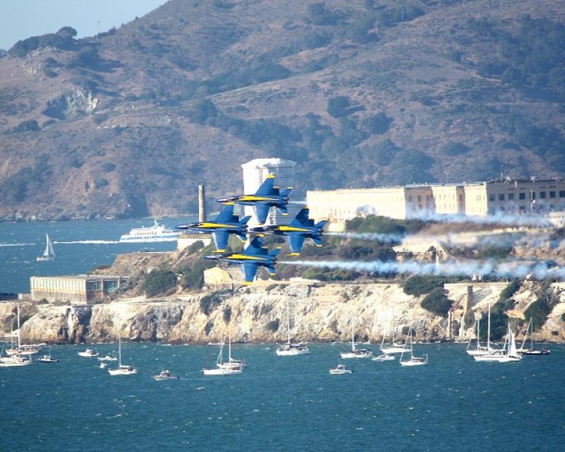 Blue Angels fighter jets in tight formation flying passed Alcatraz Island during the day.