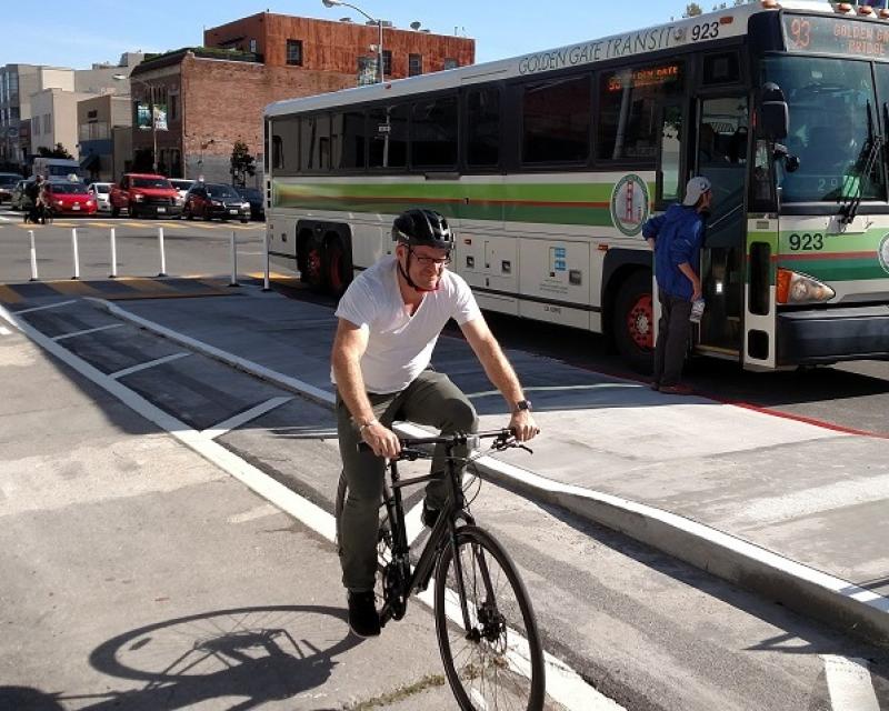Man biking in a parking-protected bike lane and transit boarding island on 7th Street.