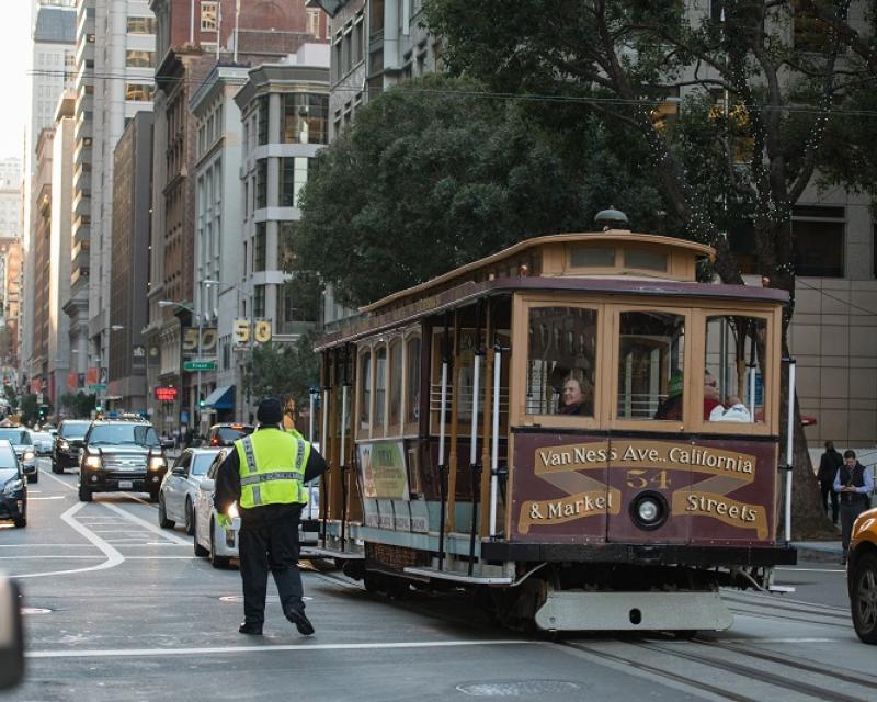 California Cable Car being guided by a parking control officer in traffic.