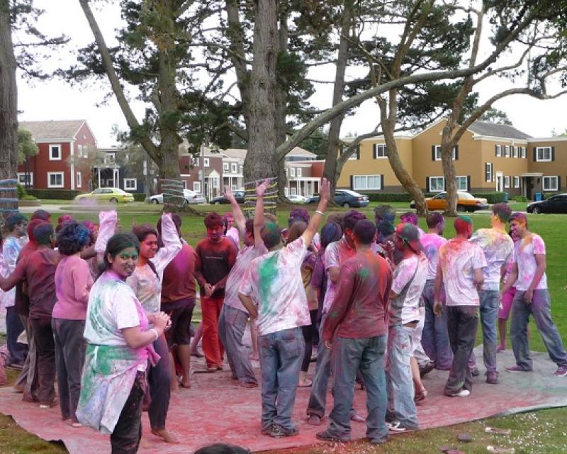 Dozens of people covers in colorful dye in the middle of a park surrounded by trees