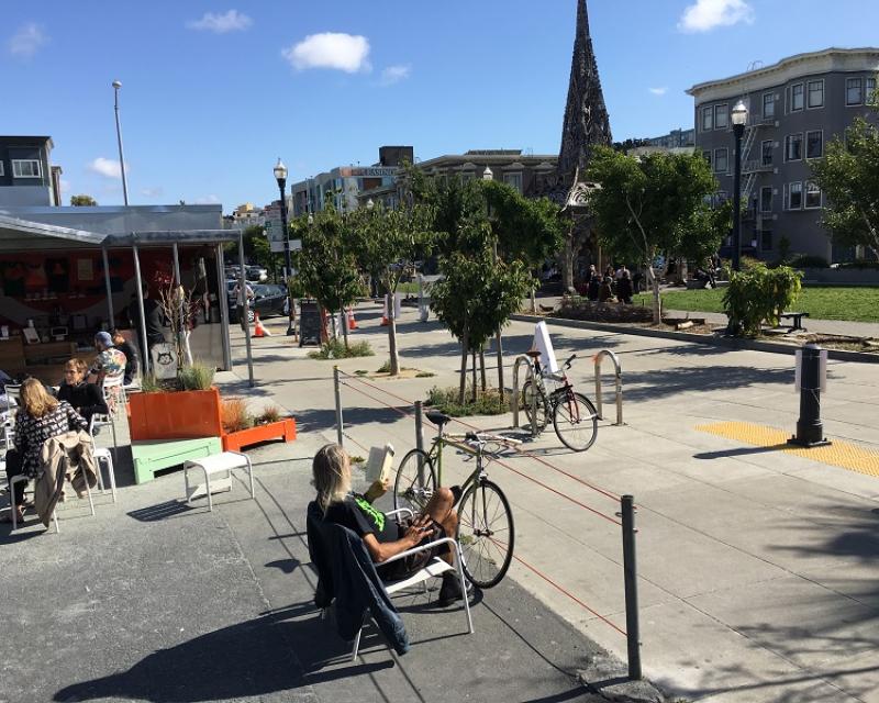 People sitting in chairs and bicycles parked in a public space next to Patricia's Green park on Octavia Street near Hayes Street.