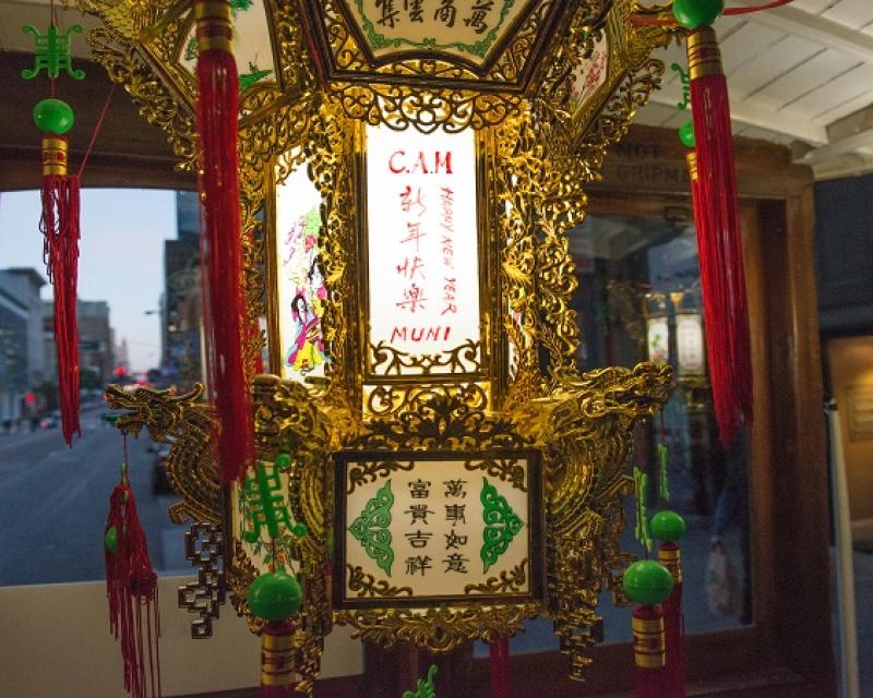 Photo of a Chinese lantern with "CAM," "Happy New Year" and "Muni" written in English next to Chinese characters, on the inside of a motorized cable car.