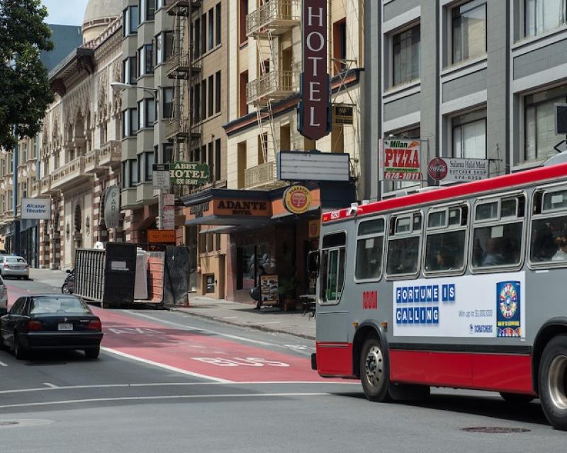 A Muni bus travels down a red transit-only lane on downtown Geary Street as cars travel in the adjacent traffic lanes.